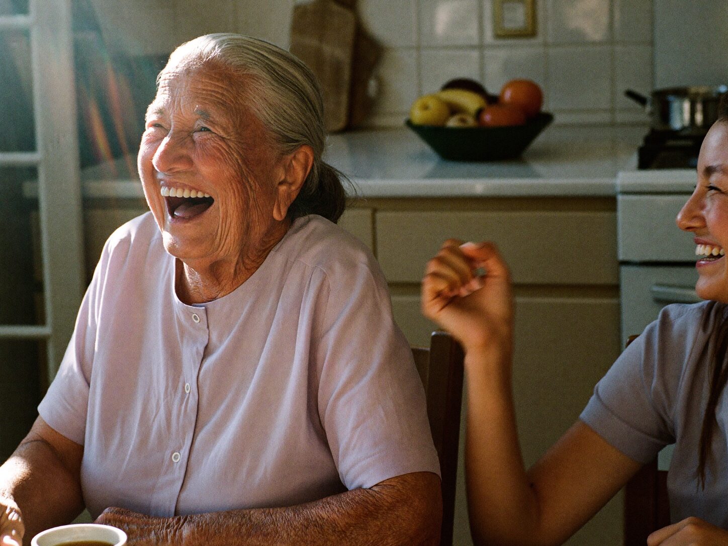 Abuela riendo con su hija mientras toman café en la cocina